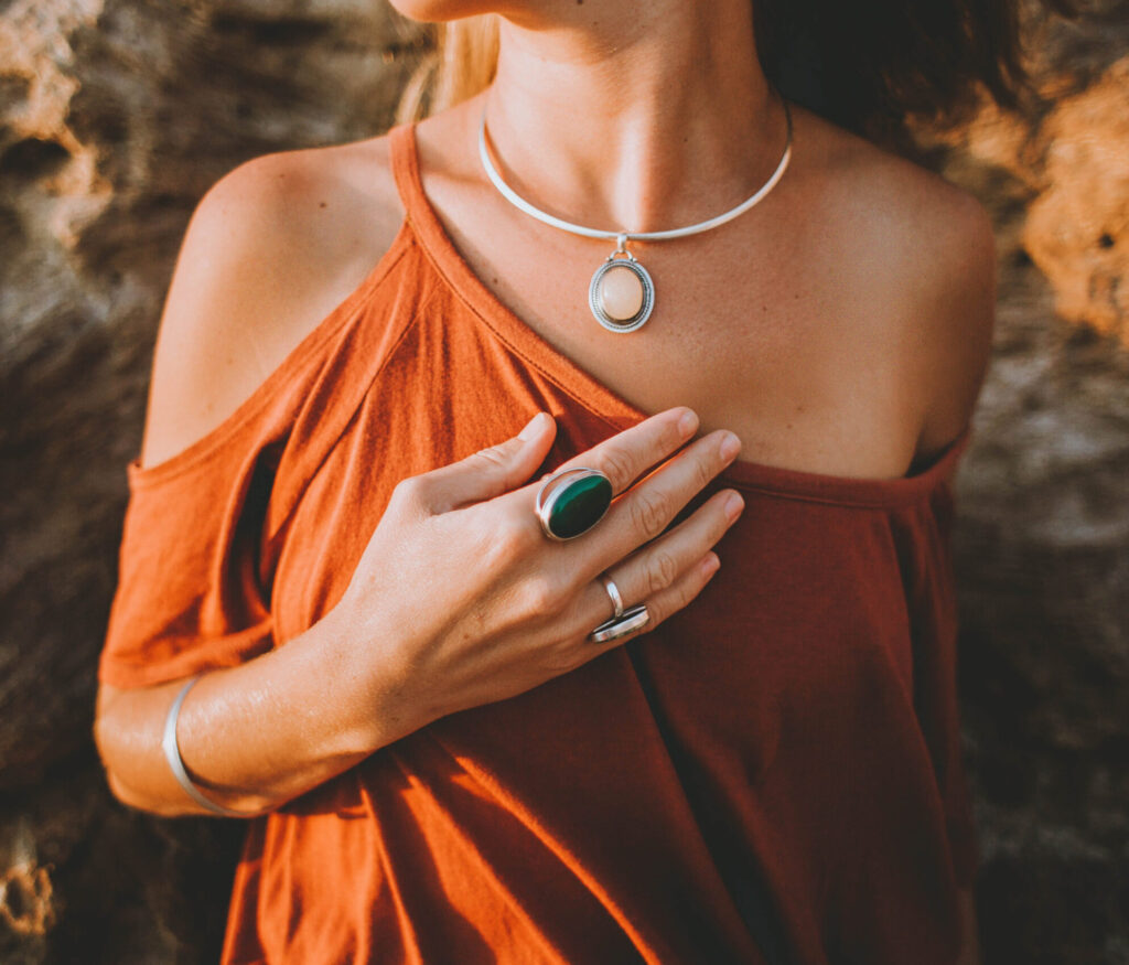 Ästhetisches Bild einer Frau mit Hand auf der Brust mit großen Stein Ringen und Kette als Sinnbild für mutiges Unternehmertum.